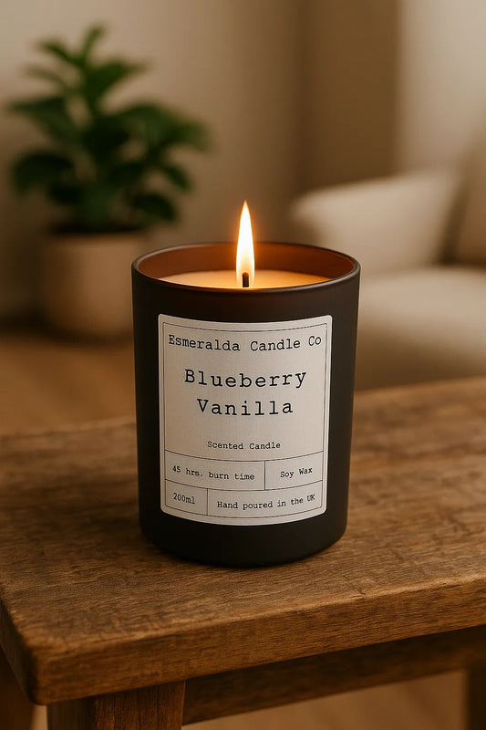 Lit Blueberry Vanilla scented candle from Esmeralda Candle Co on a wooden table, with warm ambient lighting in a cosy living room