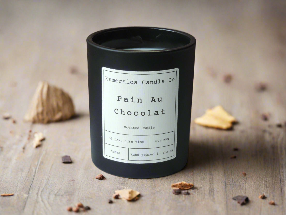 Black candle with a label on a brown surface and wooden background with crumbs of chocolate