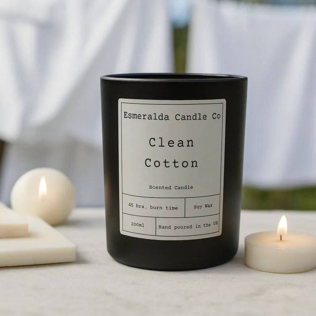 Esmeralda Candle Co Clean Cotton scented candle in a black matte jar, styled with soft white linens to reflect a fresh, airy fragrance.