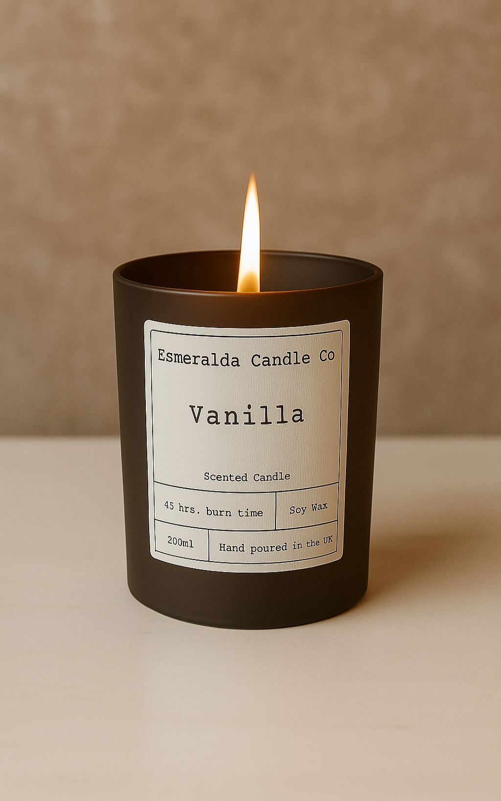 A lit Vanilla scented candle from Esmeralda Candle Co in a black glass jar with a white label, showing 45 hrs. burn time, Soy Wax, 200ml, and Hand poured in the UK