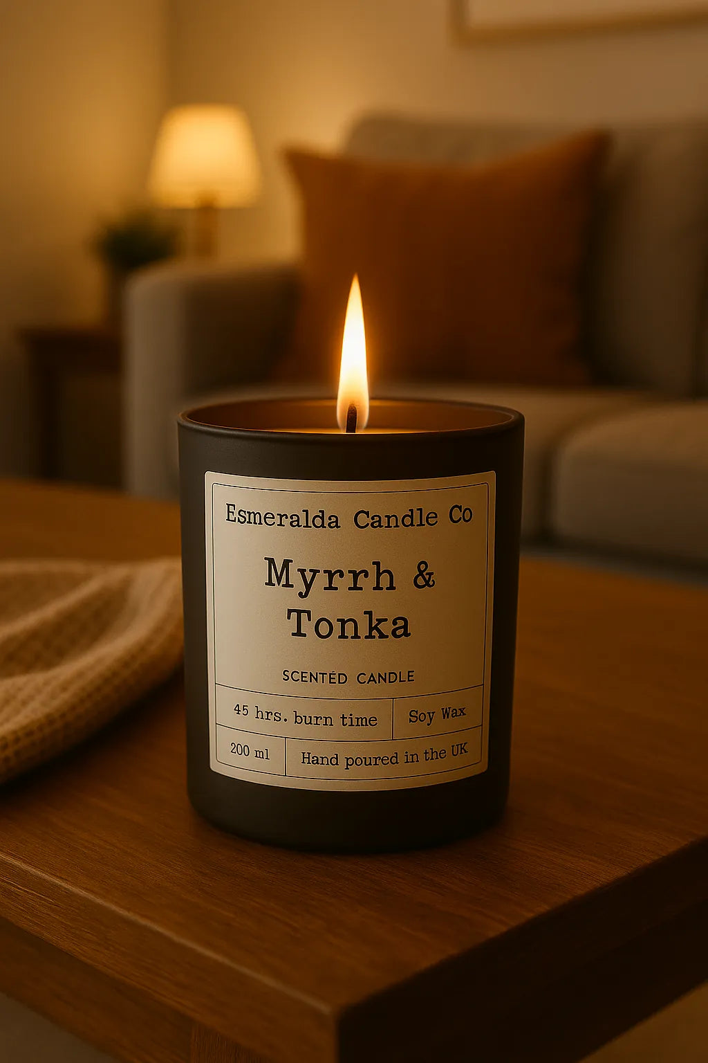 Lit Myrrh & Tonka scented candle in a matte black jar on a wooden table in a cosy living room setting.