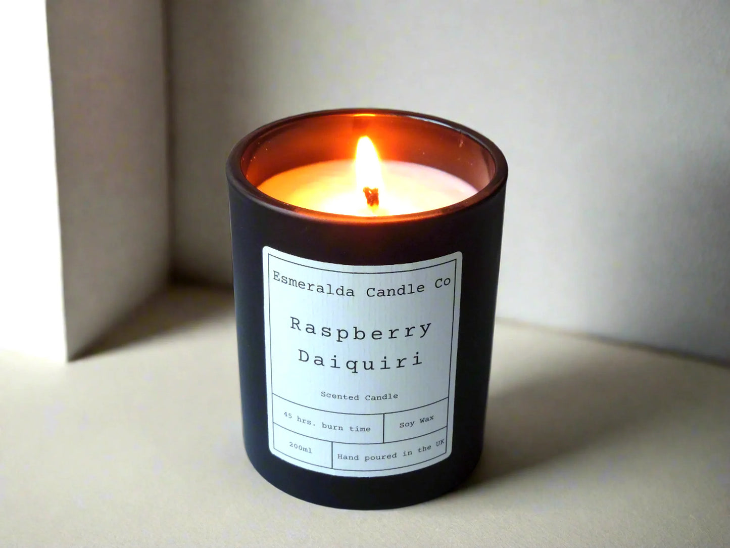Raspberry Daiquiri scented candle by Esmeralda Candle Co, 200ml soy wax in a matte black jar with 45-hour burn time, hand poured in the UK, lit and styled in a soft neutral setting.