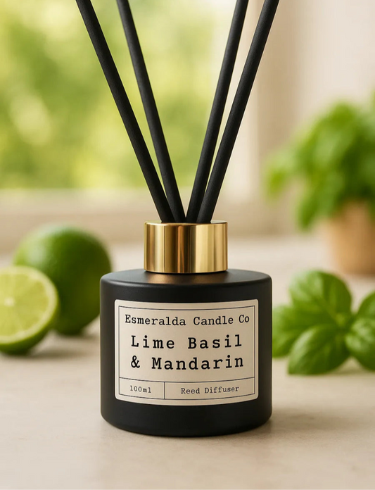 Black reed diffuser labelled 'Esmeralda Candle Co - Lime Basil & Mandarin' with black sticks, placed on a wooden surface with blurred background decor.