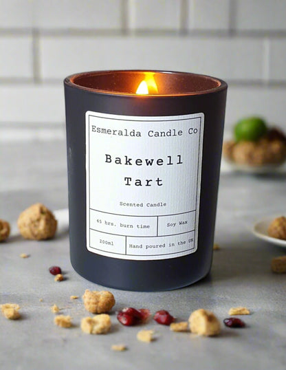Black candle with a label on a desk, lit and casting a warm glow.