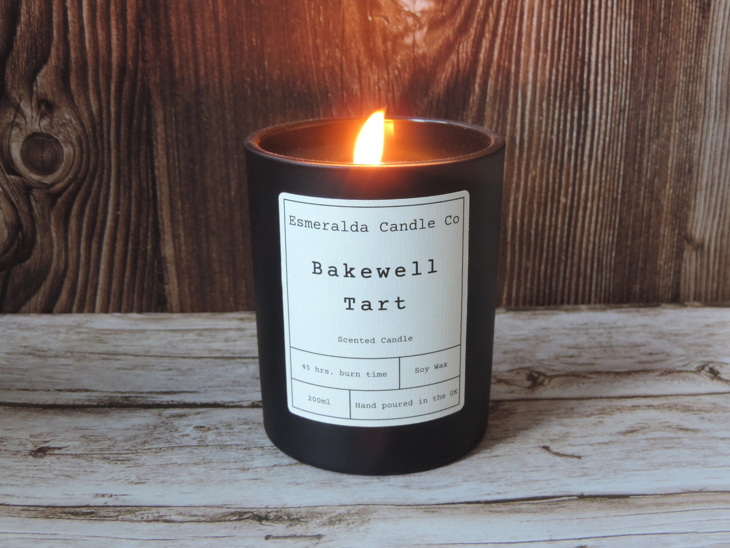 bakewell tart scented candle in matt black glass candle, on a wooden shelf