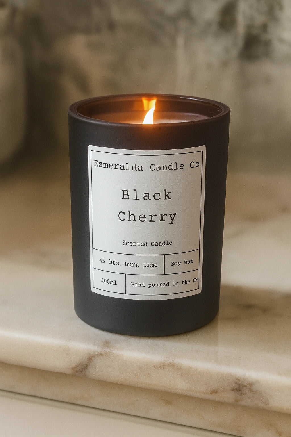 Esmeralda Candle Co Black Cherry scented candle in a black jar with warm flame, 45 hours burn time, 200ml hand-poured soy wax, displayed on a marble surface.