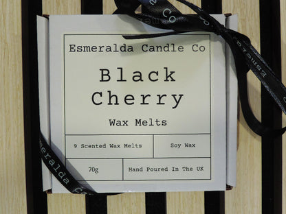 "A white gift box labelled 'Esmeralda Candle Co – Black Cherry Wax Melts' with a black ribbon, displayed on a striped wooden surface.