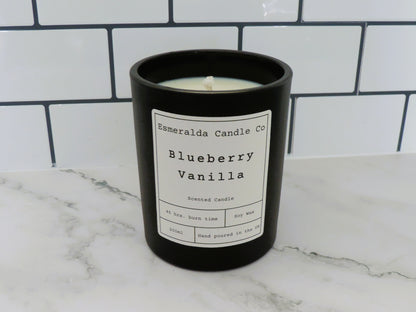  "Esmeralda Candle Co Blueberry Vanilla scented candle in a black jar, 200ml soy wax with 45-hour burn time, hand poured in the UK, displayed on a marble surface with white subway tile background.