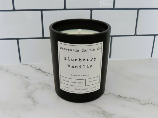  "Esmeralda Candle Co Blueberry Vanilla scented candle in a black jar, 200ml soy wax with 45-hour burn time, hand poured in the UK, displayed on a marble surface with white subway tile background.