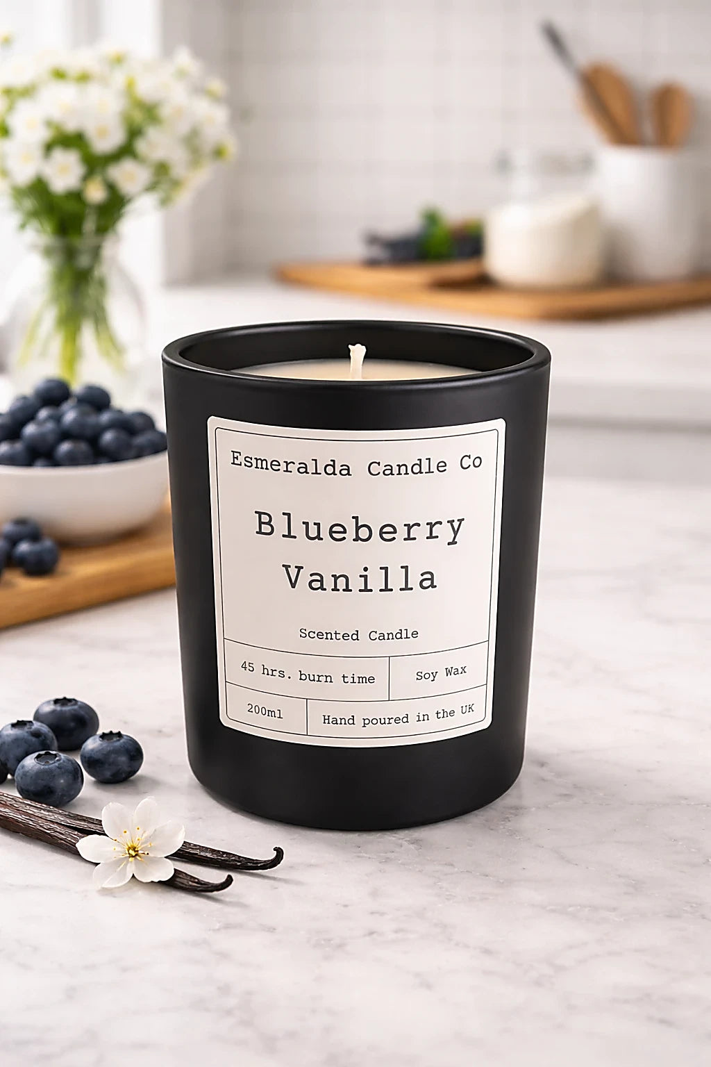 Black candle with 'Esmeralda Candle Co' label on a countertop with blueberries and vanilla beans.