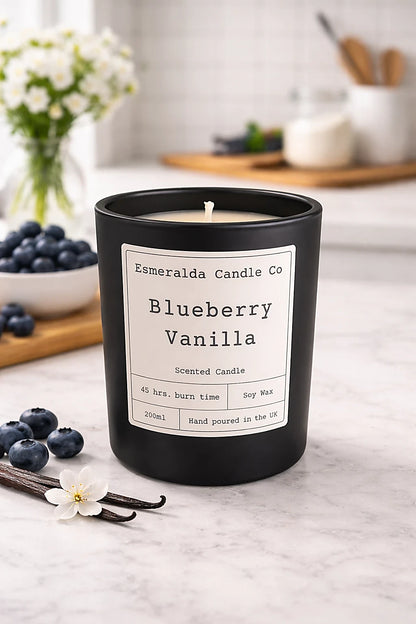 Black candle with 'Esmeralda Candle Co' label on a countertop with blueberries and vanilla beans.