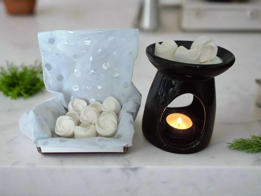 Esmeralda Candle Co white rose-shaped wax melts in a gift box and melting in a black ceramic wax warmer with a tealight candle, on a marble countertop.
