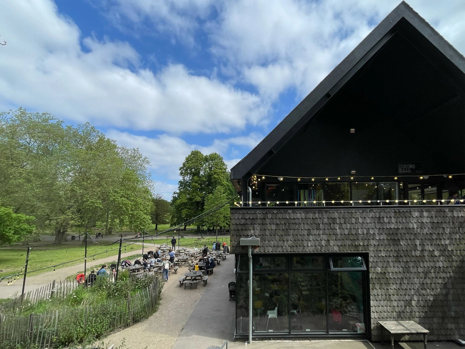 Exterior of Brown & Green Life Café at Crystal Palace Park with outdoor seating area under string lights.
