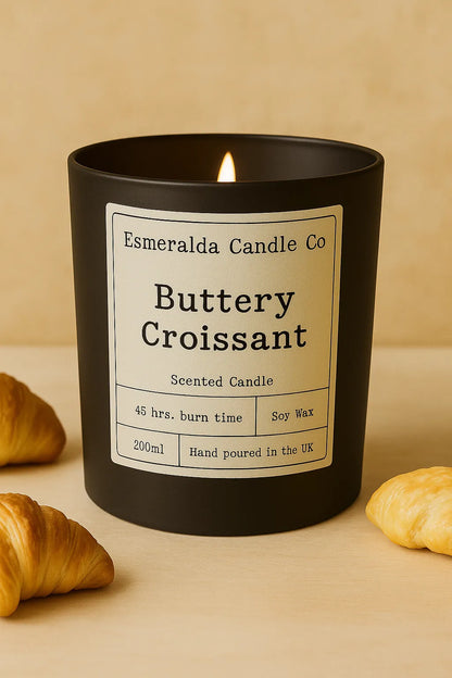 Esmeralda Candle Co Buttery Croissant scented soy wax candle in a matte black jar, 200ml with 45-hour burn time, hand poured in the UK, styled with a real croissant and pastry on a neutral background.