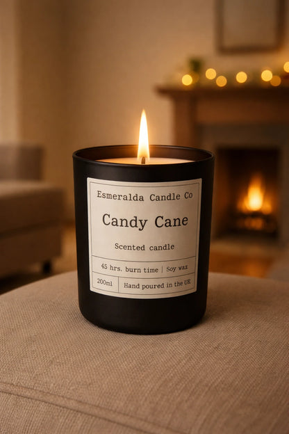 A lit Candy Cane scented candle by Esmeralda Candle Co in a matte black jar, styled on a soft neutral surface with warm ambient lighting.