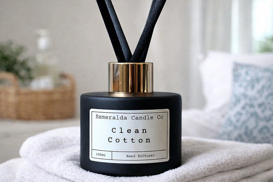 Esmeralda Candle Co Clean Cotton reed diffuser in a matte black bottle with gold collar and black reeds, 100ml home fragrance product on a light blue background.