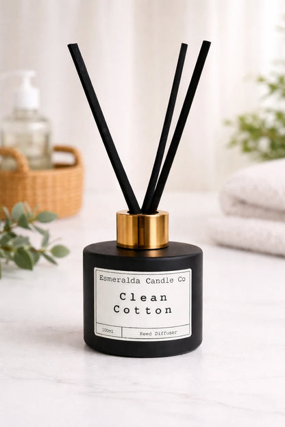 Esmeralda Candle Co Clean Cotton reed diffuser in a matte black bottle with gold collar and black reeds, 100ml home fragrance product on a light blue background.