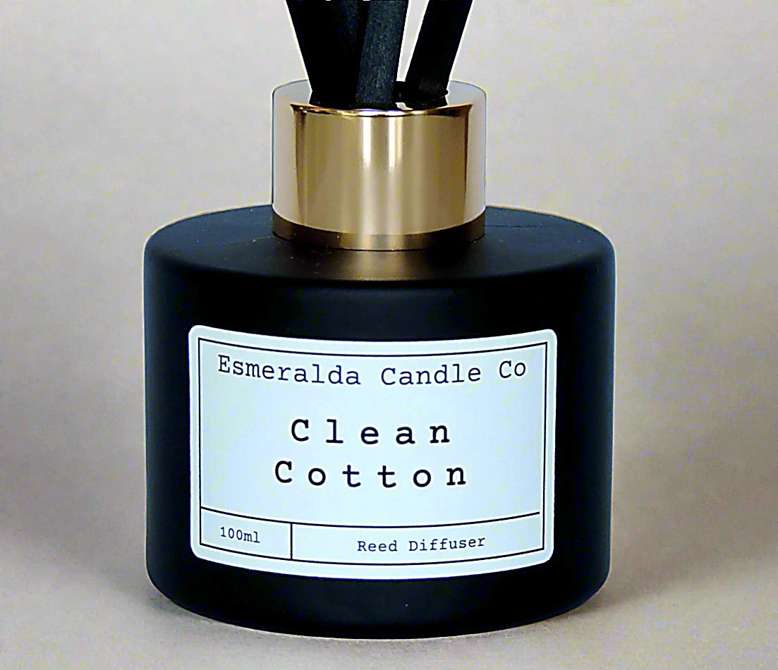 Esmeralda Candle Co Clean Cotton reed diffuser in a matte black bottle with gold collar and black reeds, 100ml home fragrance product on a light blue background.