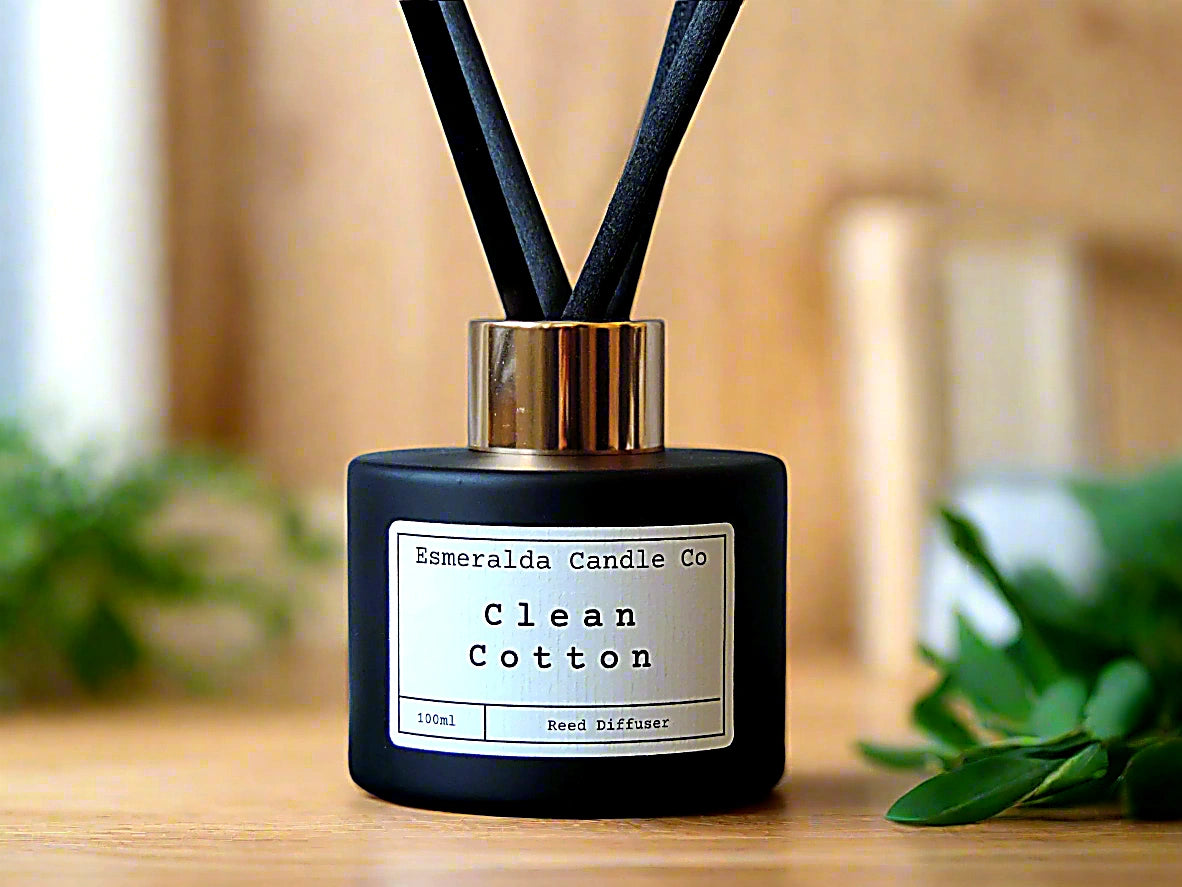 Clean Cotton reed diffuser by Esmeralda Candle Co, 100ml matte black bottle with gold collar and black reeds, styled against silver fabric for a fresh, airy home fragrance look.