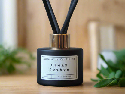Clean Cotton reed diffuser by Esmeralda Candle Co, 100ml matte black bottle with gold collar and black reeds, styled against silver fabric for a fresh, airy home fragrance look.