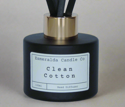 Esmeralda Candle Co Clean Cotton reed diffuser in a matte black bottle with gold collar and black reeds, 100ml home fragrance product on a light blue background.