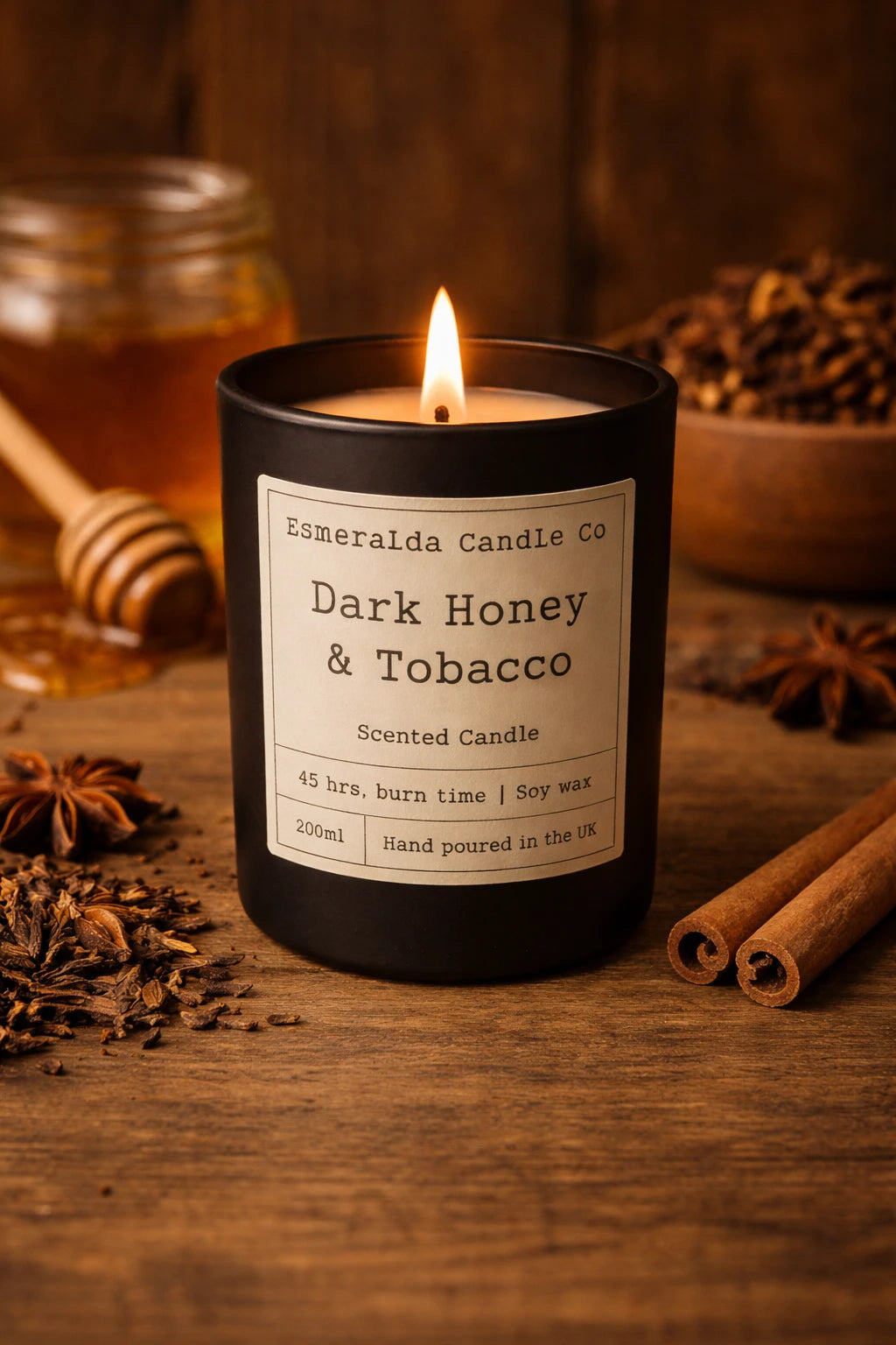 A lit Dark Honey & Tobacco scented candle in a black jar, styled with honey, spices, and warm ambient lighting.