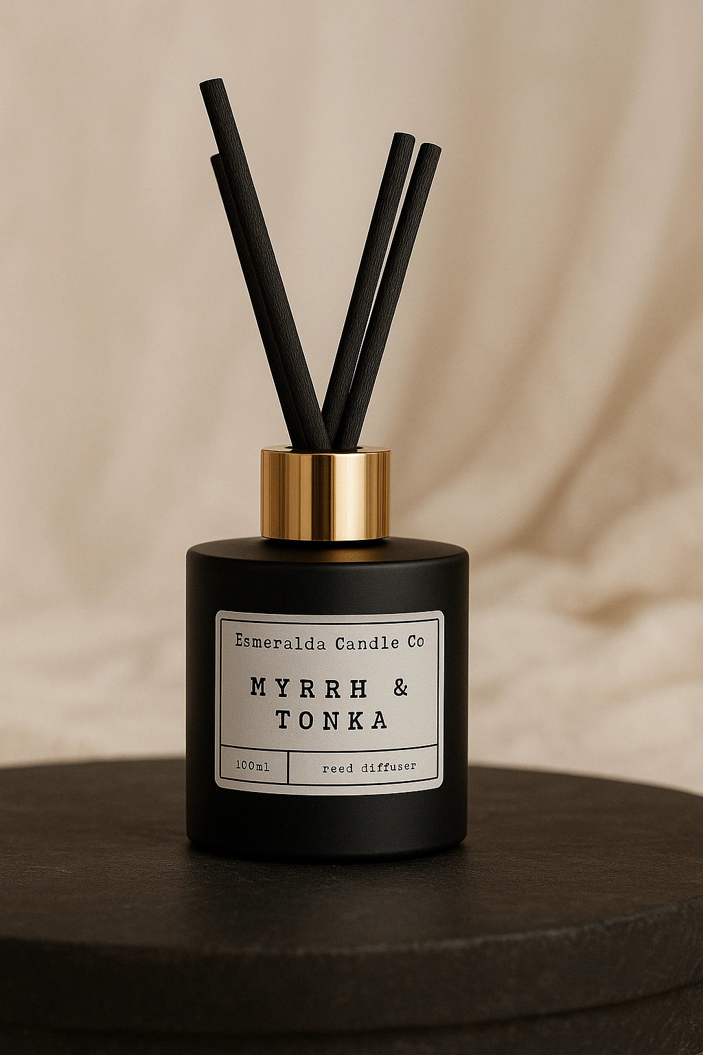 Esmeralda Candle Co Myrrh & Tonka reed diffuser in matte black bottle with gold collar and black reeds, styled against a soft cream background.
