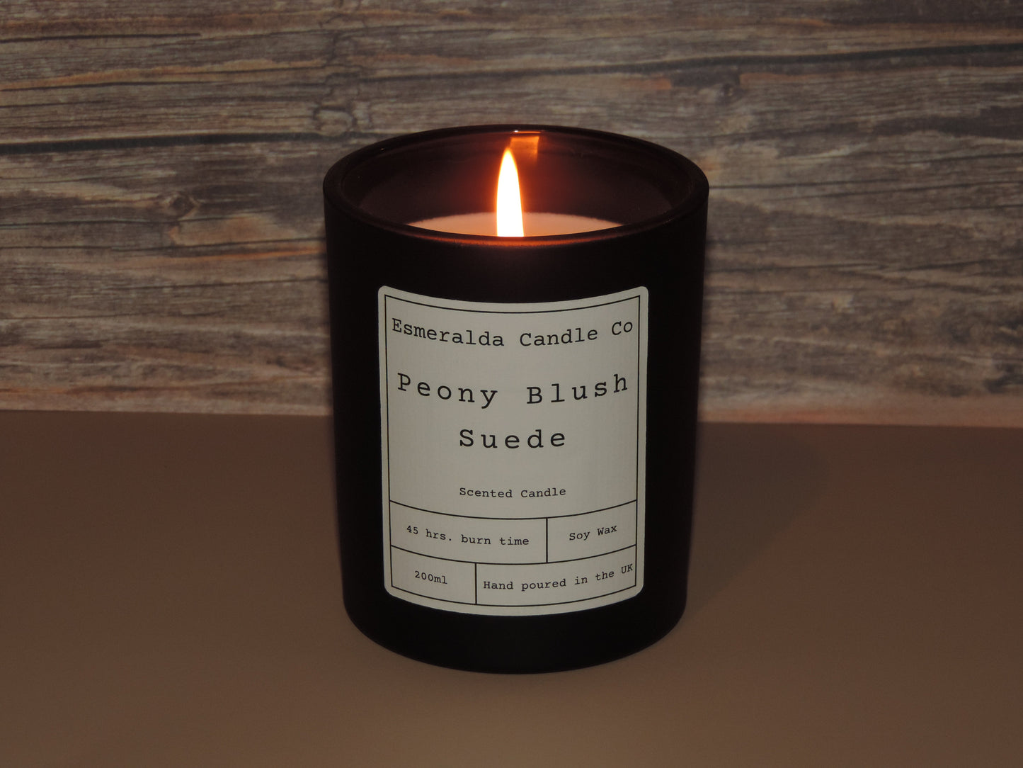 A lite scented candle on a brown back ground, with a label on that reads. Esmeralda candle co