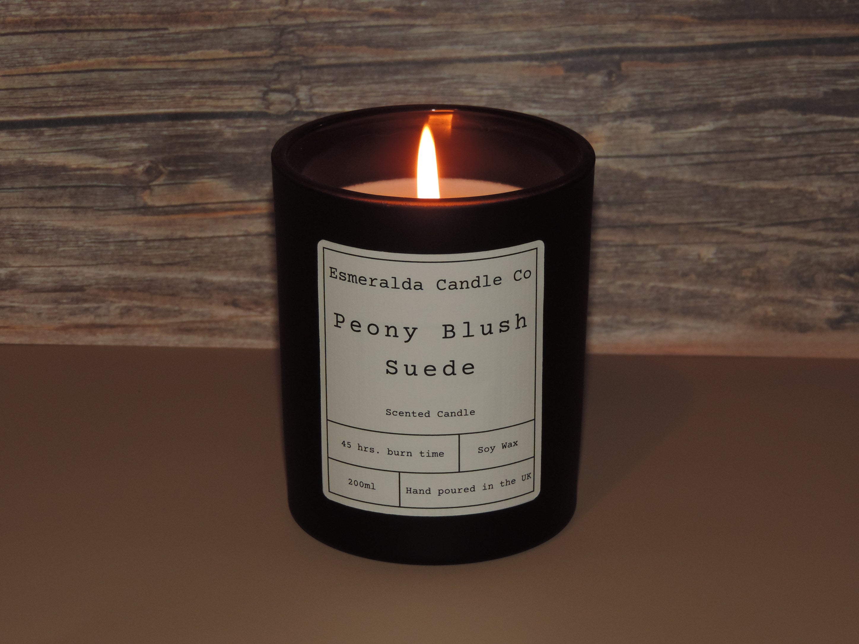 A lite scented candle on a brown back ground, with a label on that reads. Esmeralda candle co