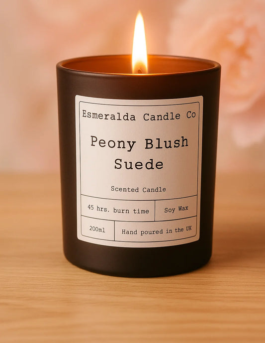 Scented candle labelled 'Peony Blush Suede' by Esmeralda Candle Co on a wooden surface.