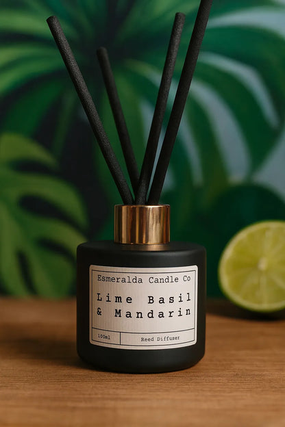 Black reed diffuser labelled 'Esmeralda Candle Co - Lime Basil & Mandarin' with black sticks, placed on a wooden surface with blurred background decor.