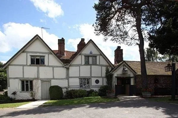 Traditional English house with a white facade and red roof, surrounded by trees and clear sky.