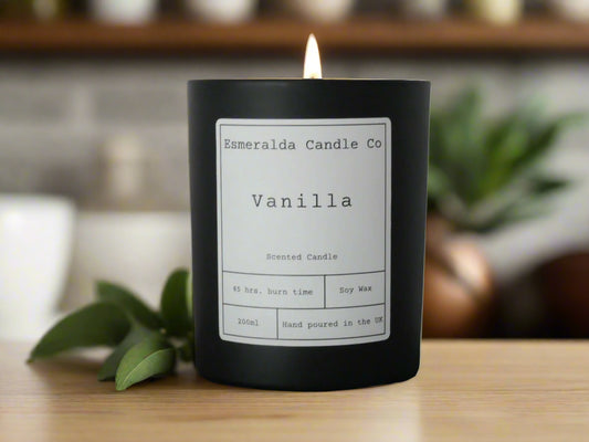 Vanilla scented candle by Esmeralda Candle Co, 200ml matte black jar with 45-hour burn time, soy wax, hand poured in the UK, lit on a marble surface for a cozy ambiance.