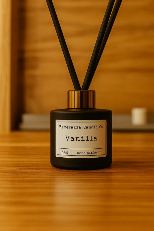Esmeralda Candle Co Vanilla reed diffuser in a matte black bottle with gold collar and black reeds, styled on a warm wooden surface with cosy lighting.