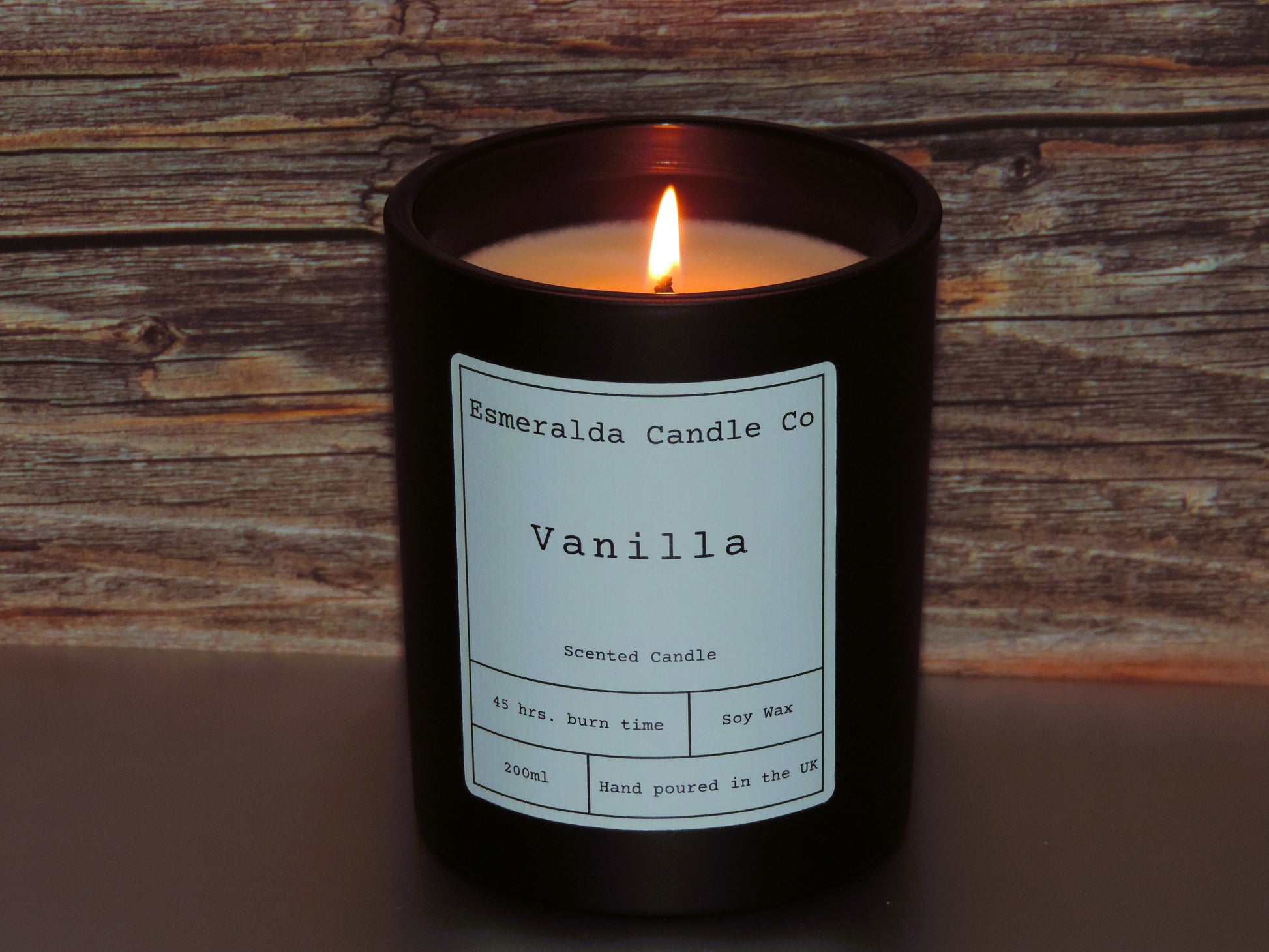 A lit candle in glass black container on a wooden shelf