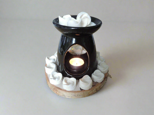 Black ceramic oil burner with a lit tealight candle, surrounded by white rose-shaped wax melts on a wooden base